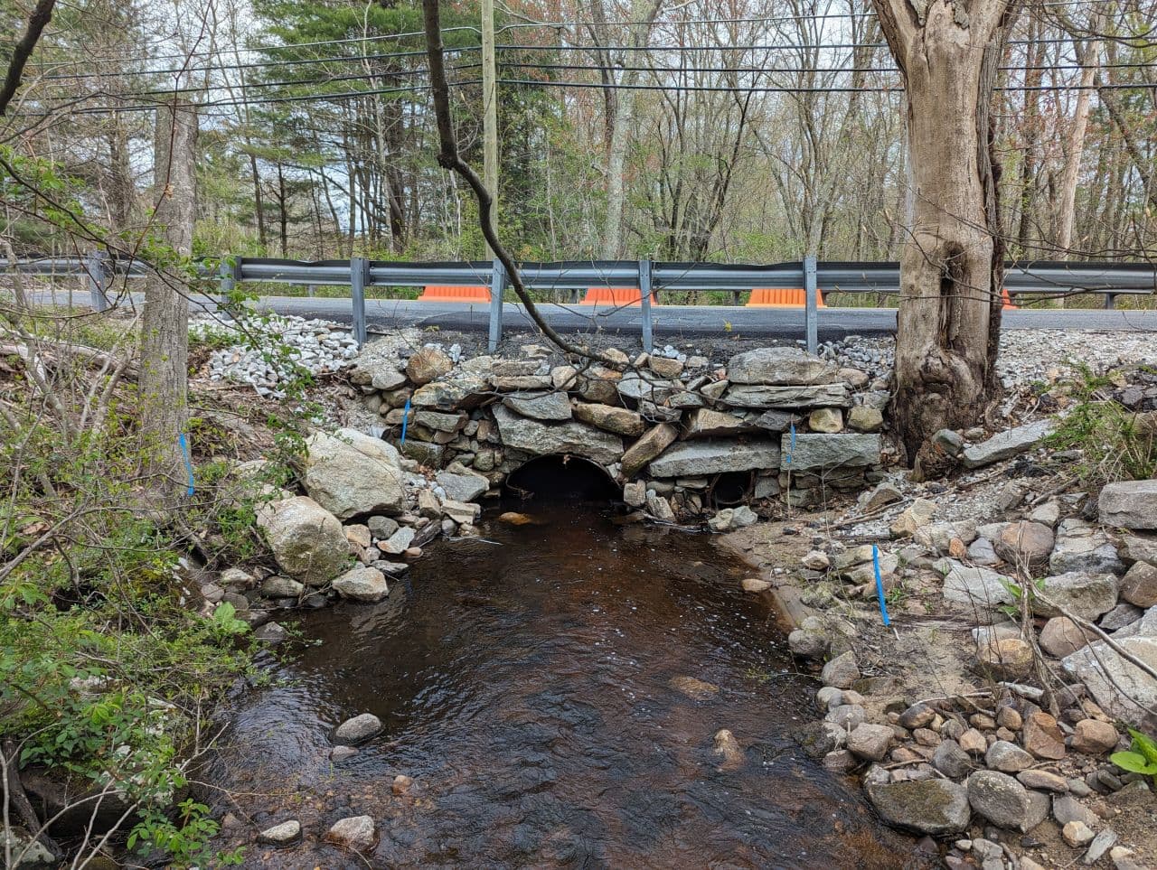 Existing Providence Street culvert: a stone arch structure carrying Spring Brook under the road, with orange traffic barriers above